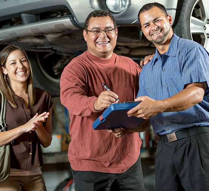 Image of a hispanic couple smiling next to a mechanic after being able to pay for their auto repair with a payment solution through American First Finance.